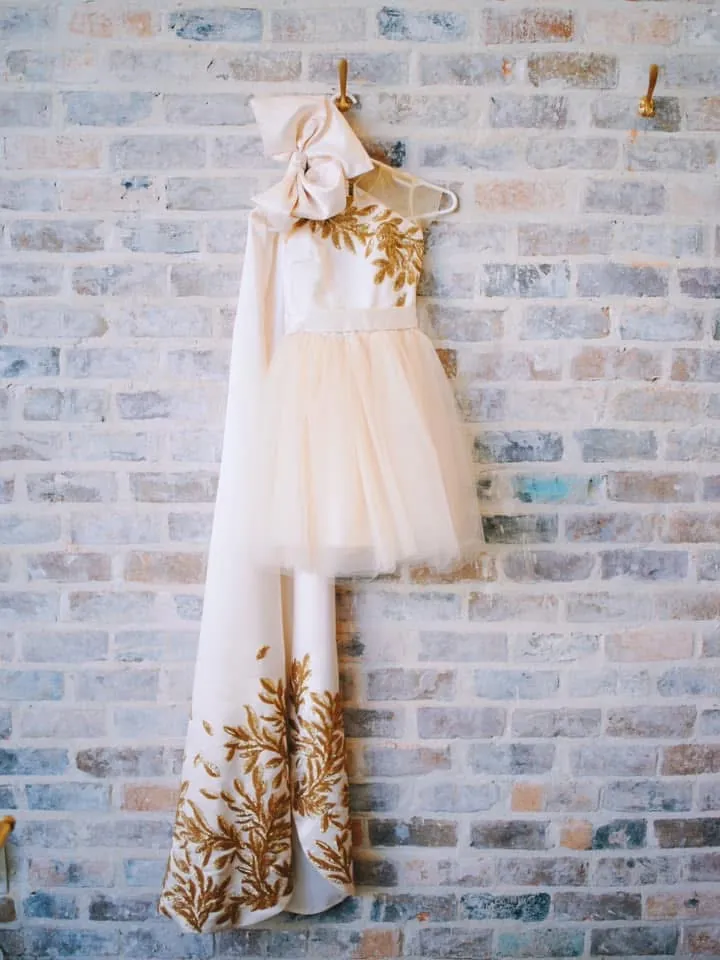 Ivory gown with gold leaf appliqué hanging on a brick wall